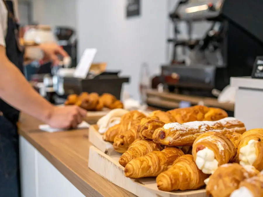 A cafe counter with croissants and cream-filled pastries in a display case