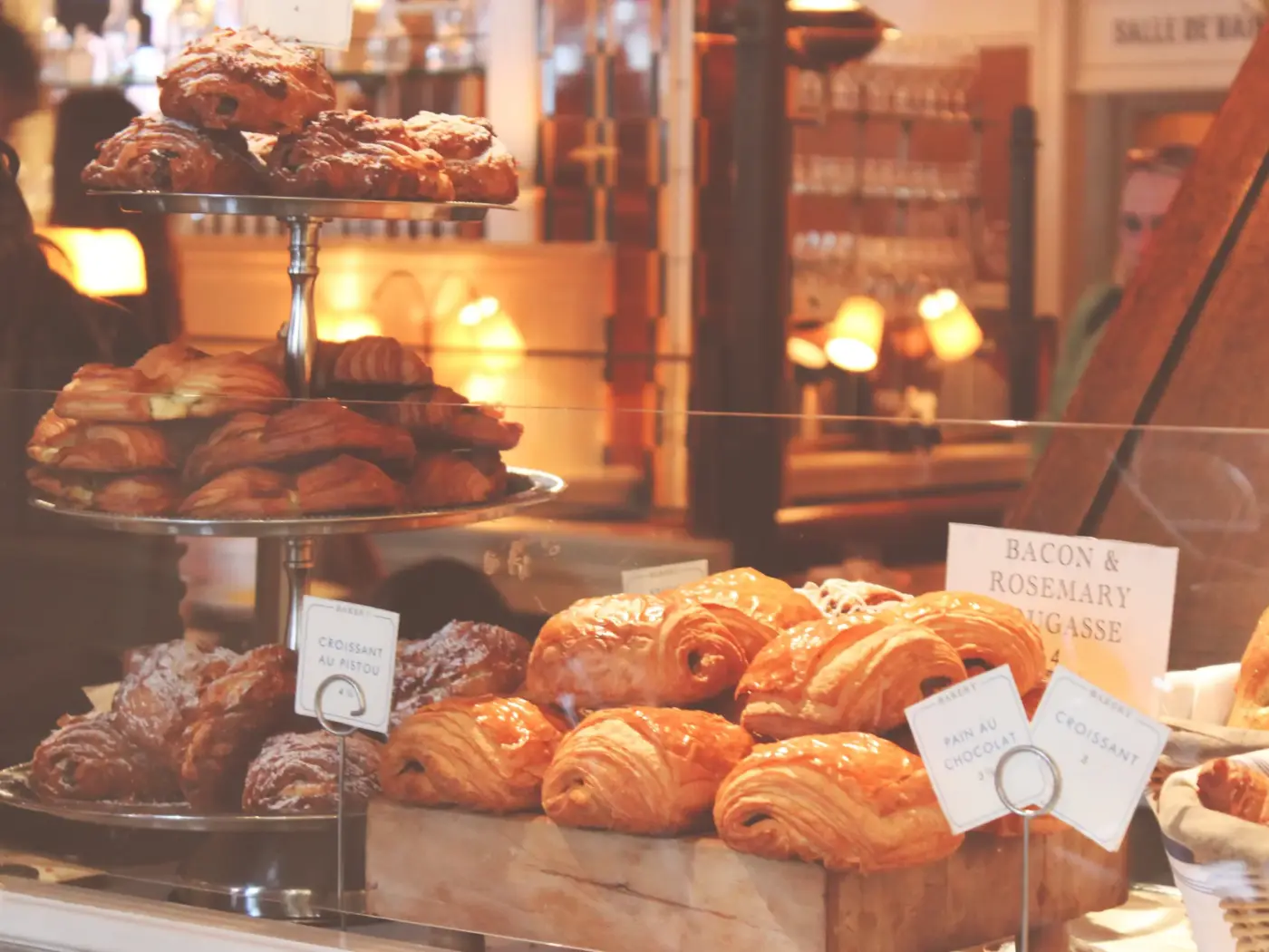 A warmly lit bakery display of croissants and pastries on tiered stands