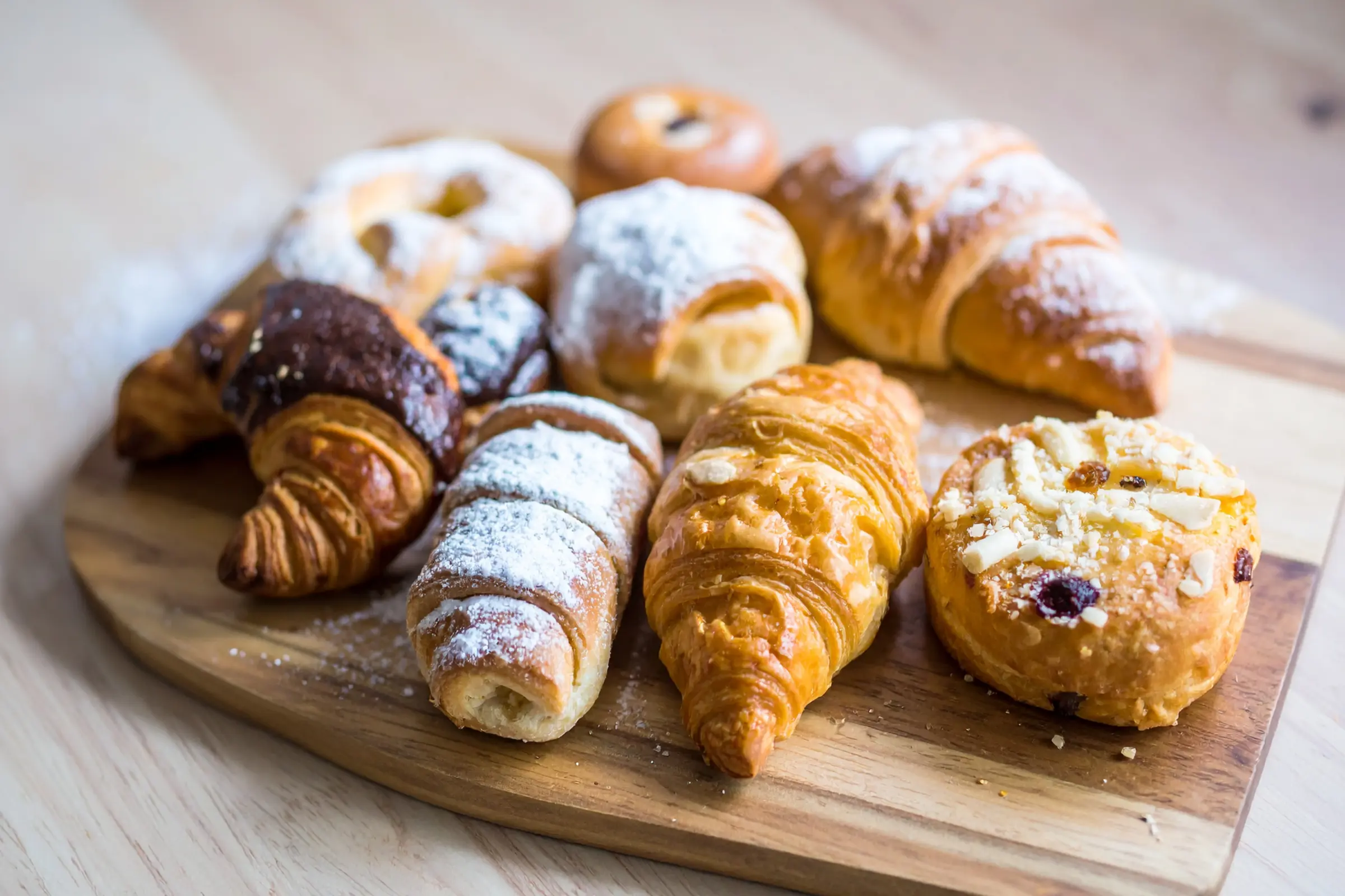 Croissants and powdered-sugar Danishes on a wood board