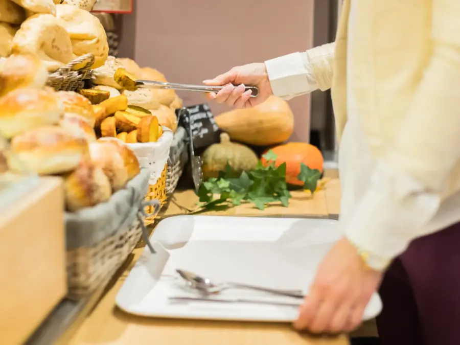 A foodservice worker plating fresh food along a buffet line