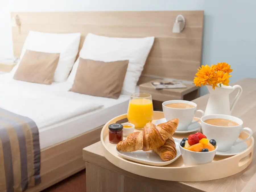 A hotel breakfast tray with juice, coffee, croissants and fruit on a bed