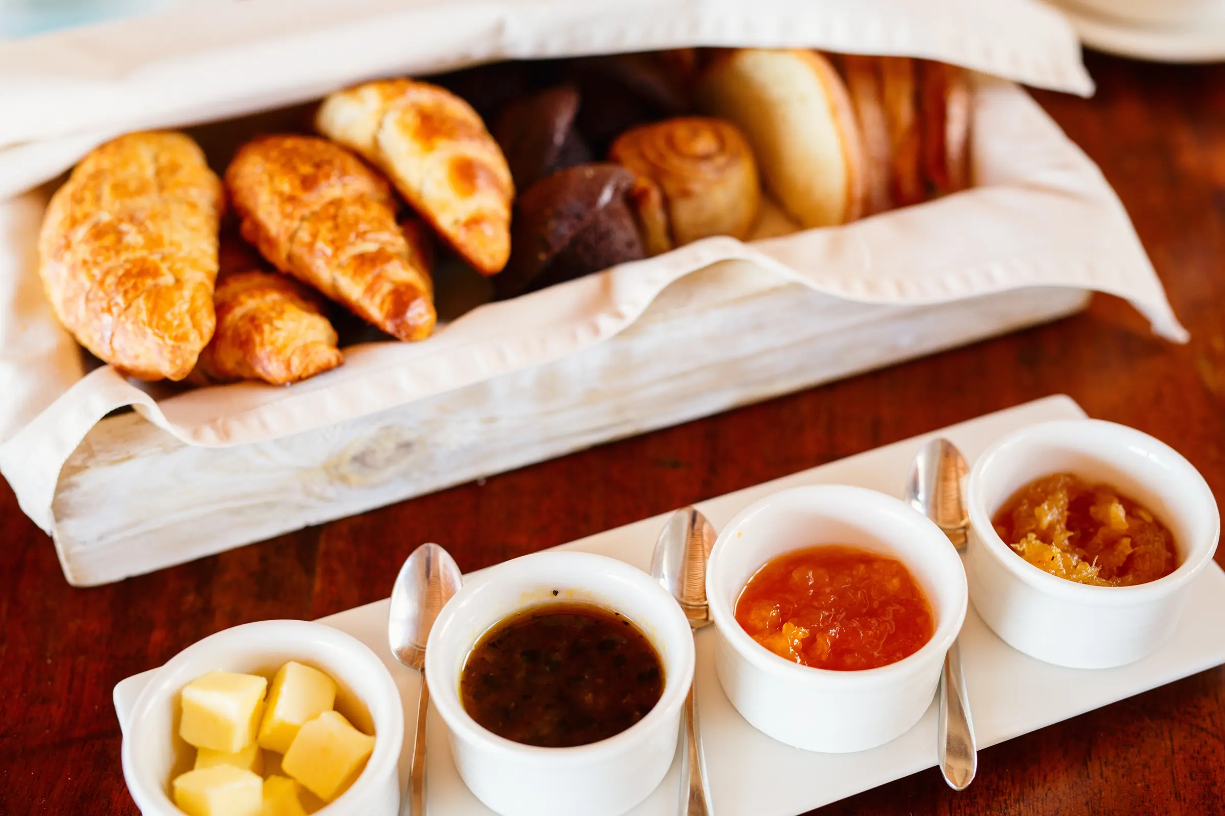 A hotel breakfast service of croissants and pastries with jam and butter